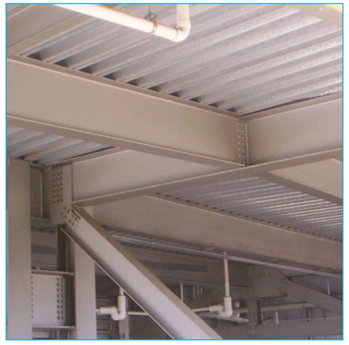 Interior view of a metal structure with beams, pipes, and a corrugated metal roof.
