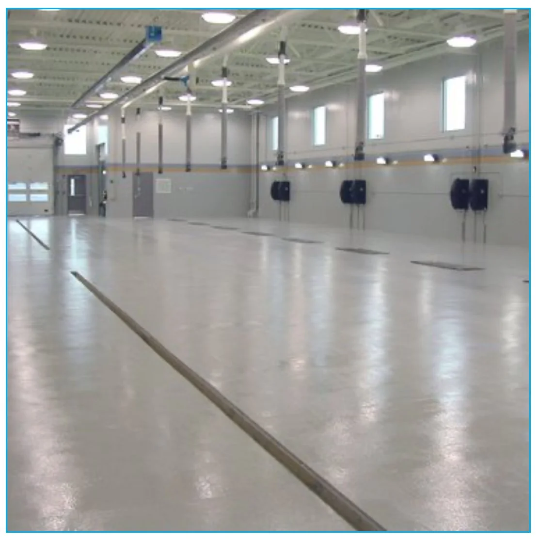 Empty industrial or warehouse space with smooth floors, high ceilings, windows, and industrial lighting.