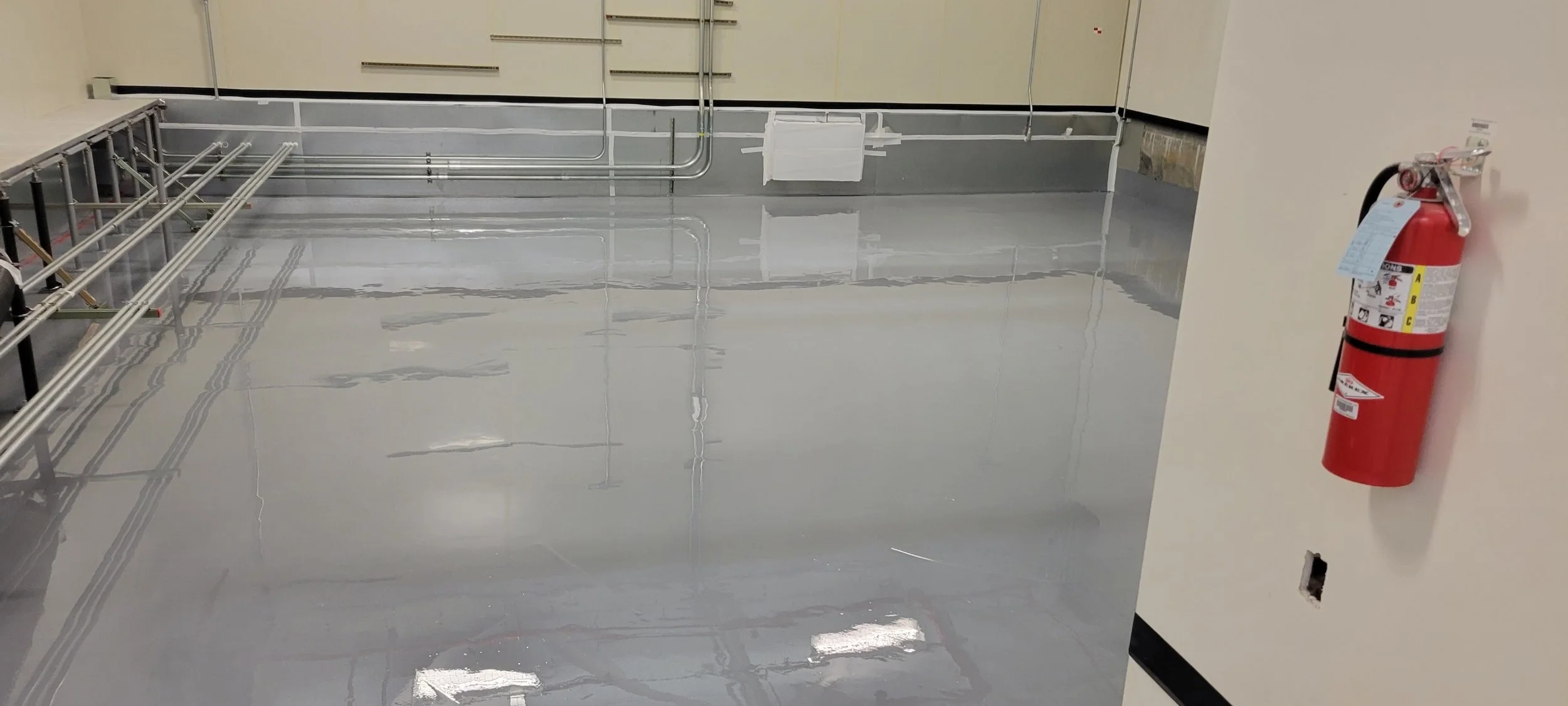 A clean, shiny epoxy-finished concrete floor in an industrial or commercial space, with a fire extinguisher mounted on the wall to the right.