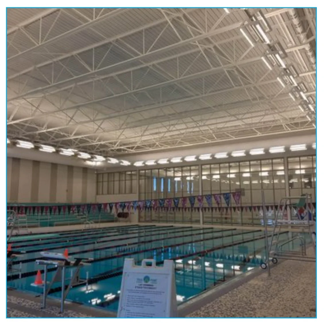 Indoor swimming pool with lane markers, colorful flags, and a lifeguard stand at the edge.