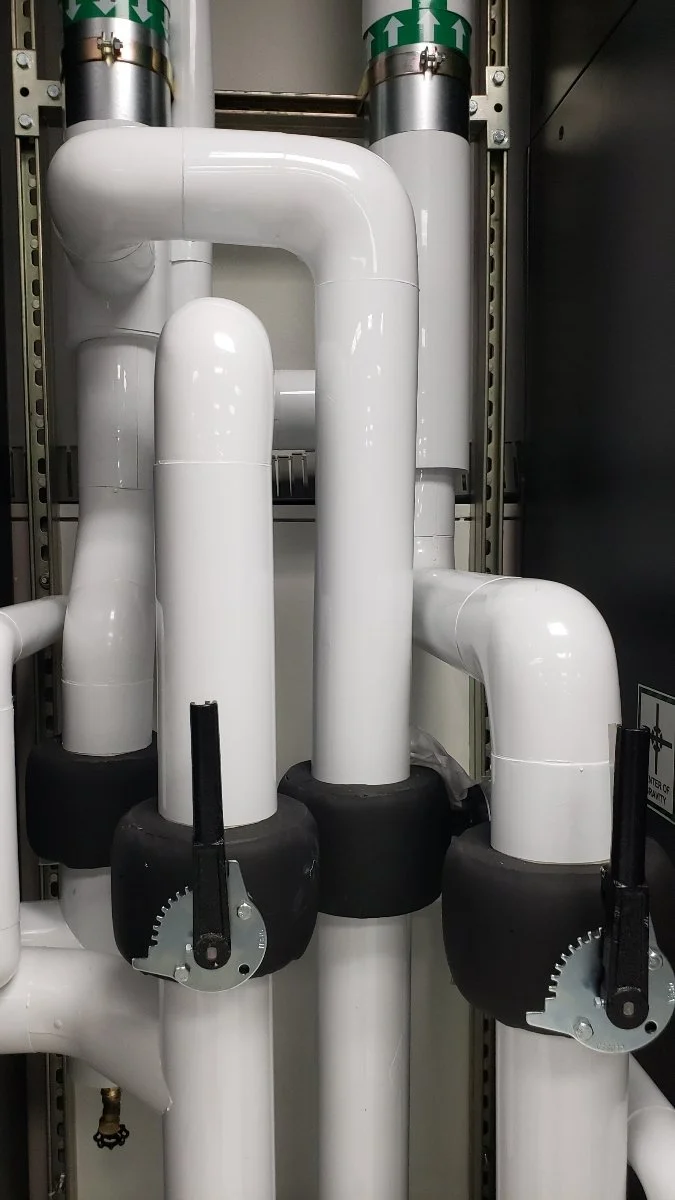 Two white pipes with black valve controls connected to black fittings, part of an industrial piping system.