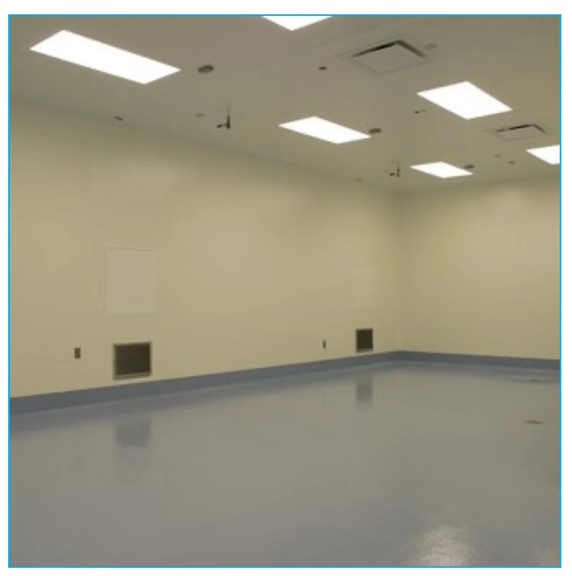 Empty room with beige walls, gray baseboards, and a shiny gray floor. The ceiling has multiple rectangular fluorescent lights and an air vent.