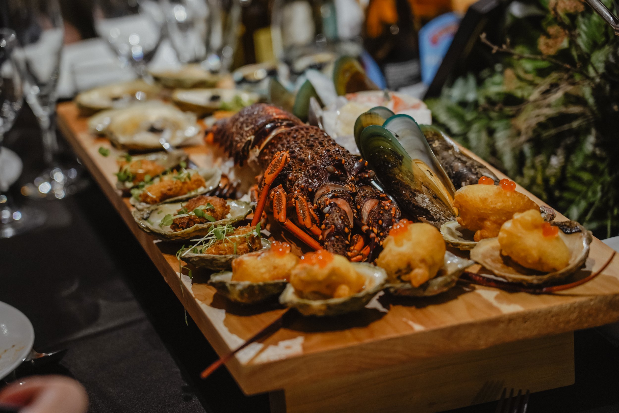 Lobster, oysters with toppings, and mussels on a wooden platter at a seafood dinner.