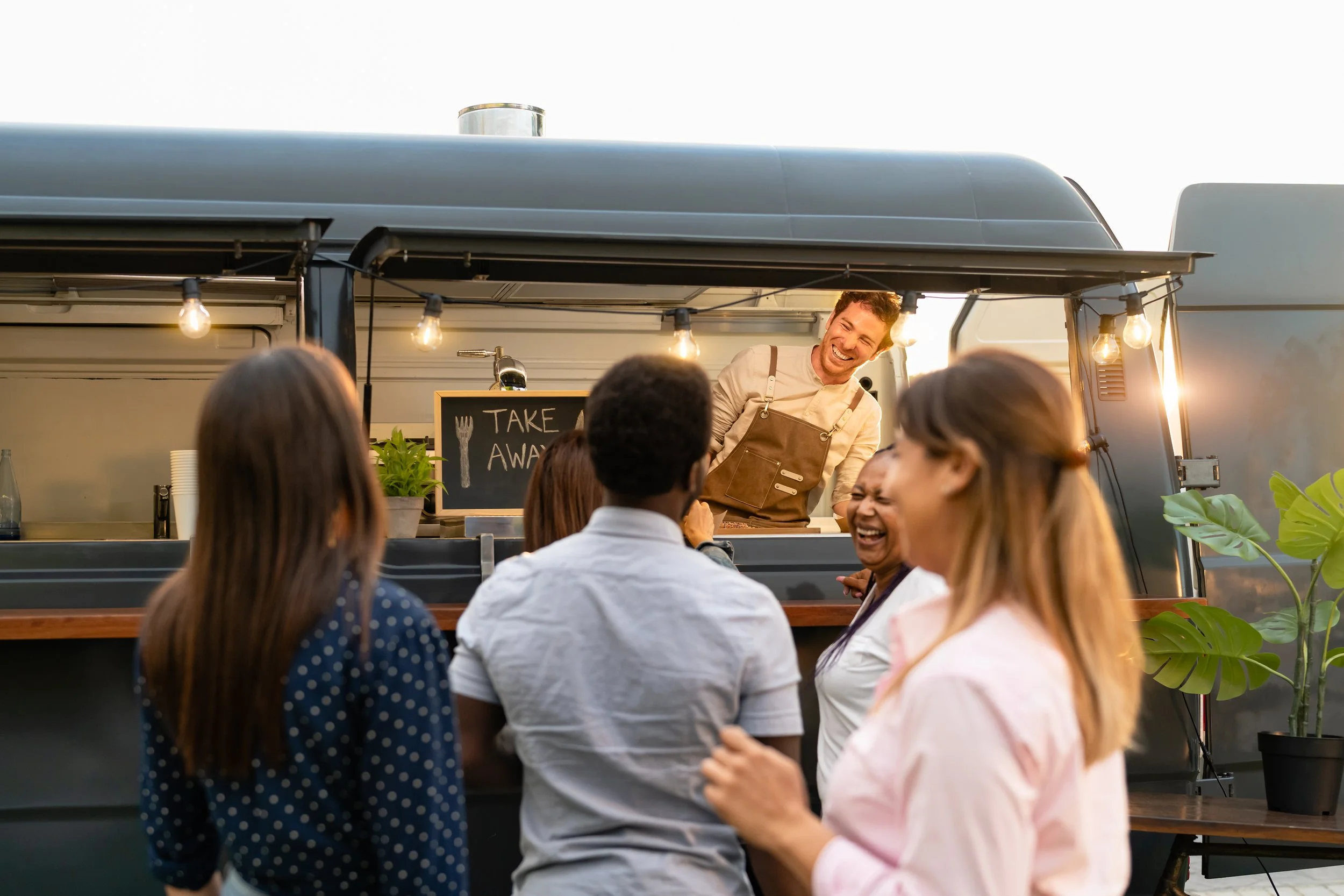 People laughing and chatting at a food truck with a smiling server.
