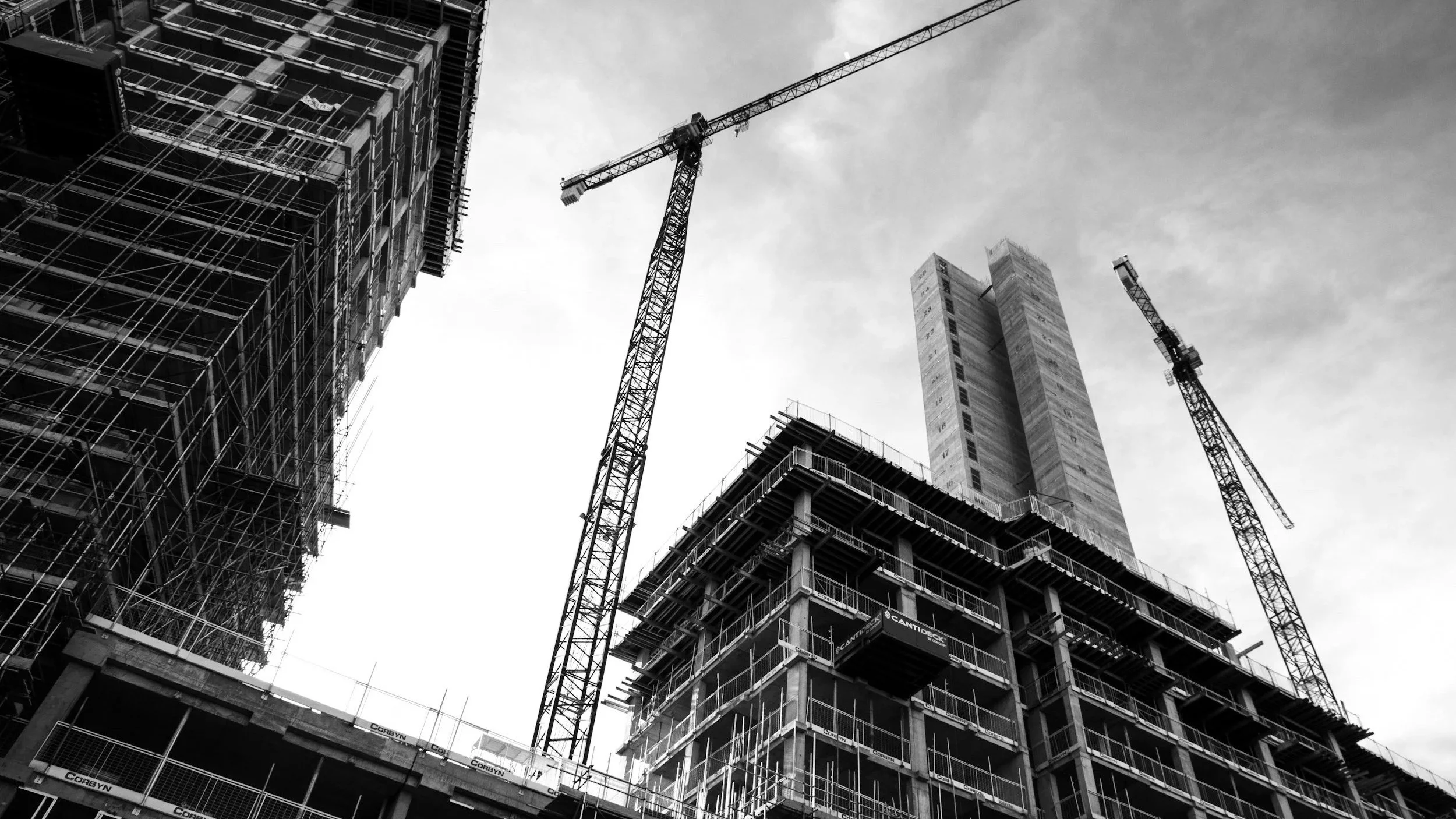Multiple tall cranes towering over a busy commercial construction site, representing large-scale infrastructure development and active building projects.