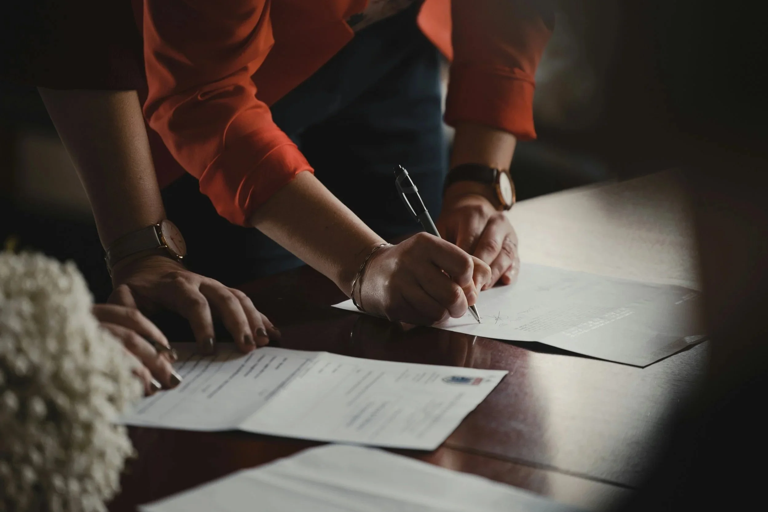 Person signing legal documents at a wooden desk, representing career decisions between law firm and in-house counsel paths