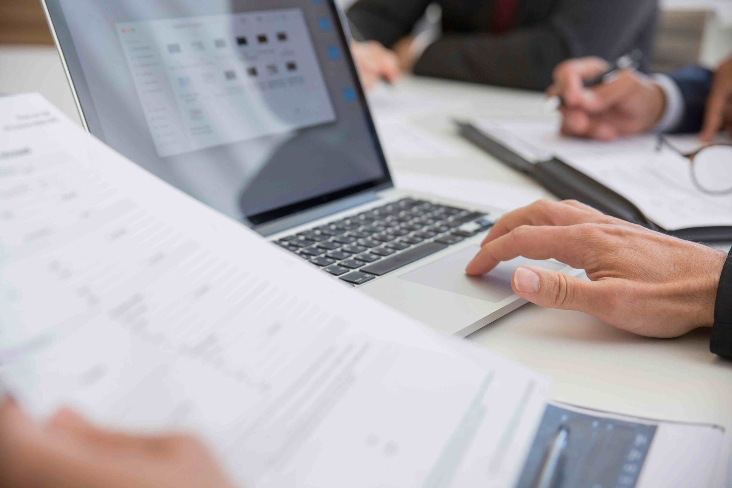 Close-up of hands working on a laptop and holding recruitment documents during a meeting at an office table.