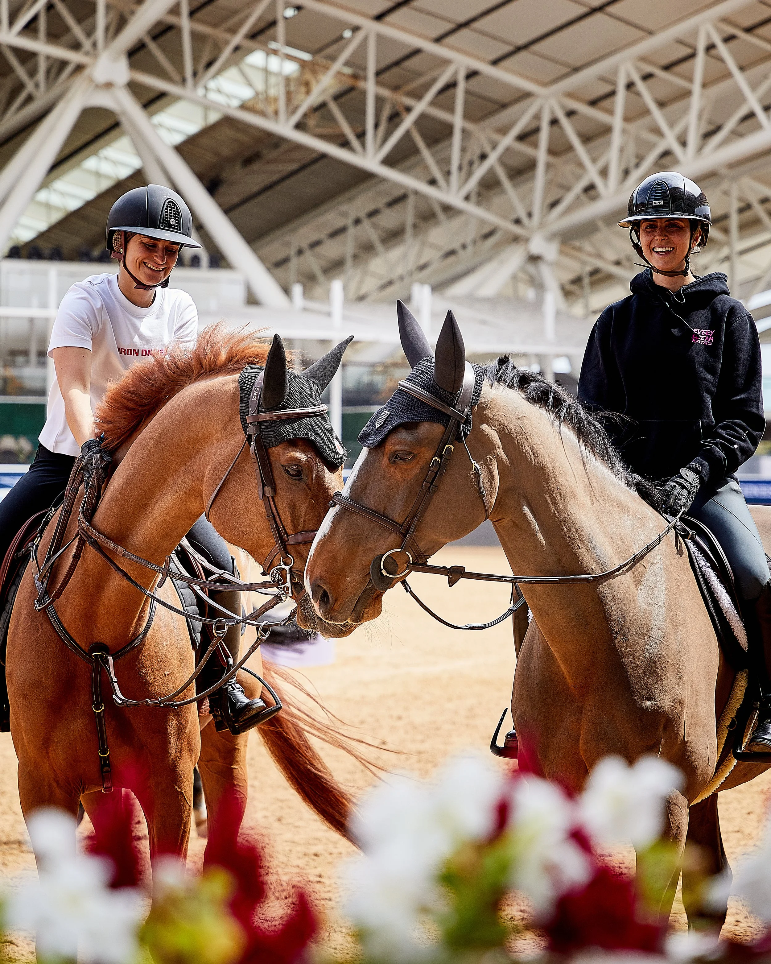 A candid photoshoot with Ioli Mytilineou and Jeanne Sadran for Iron Dames at the LGCT in Doha, Al Shaqab, they are in the warm up arena and their horses are touching noses.