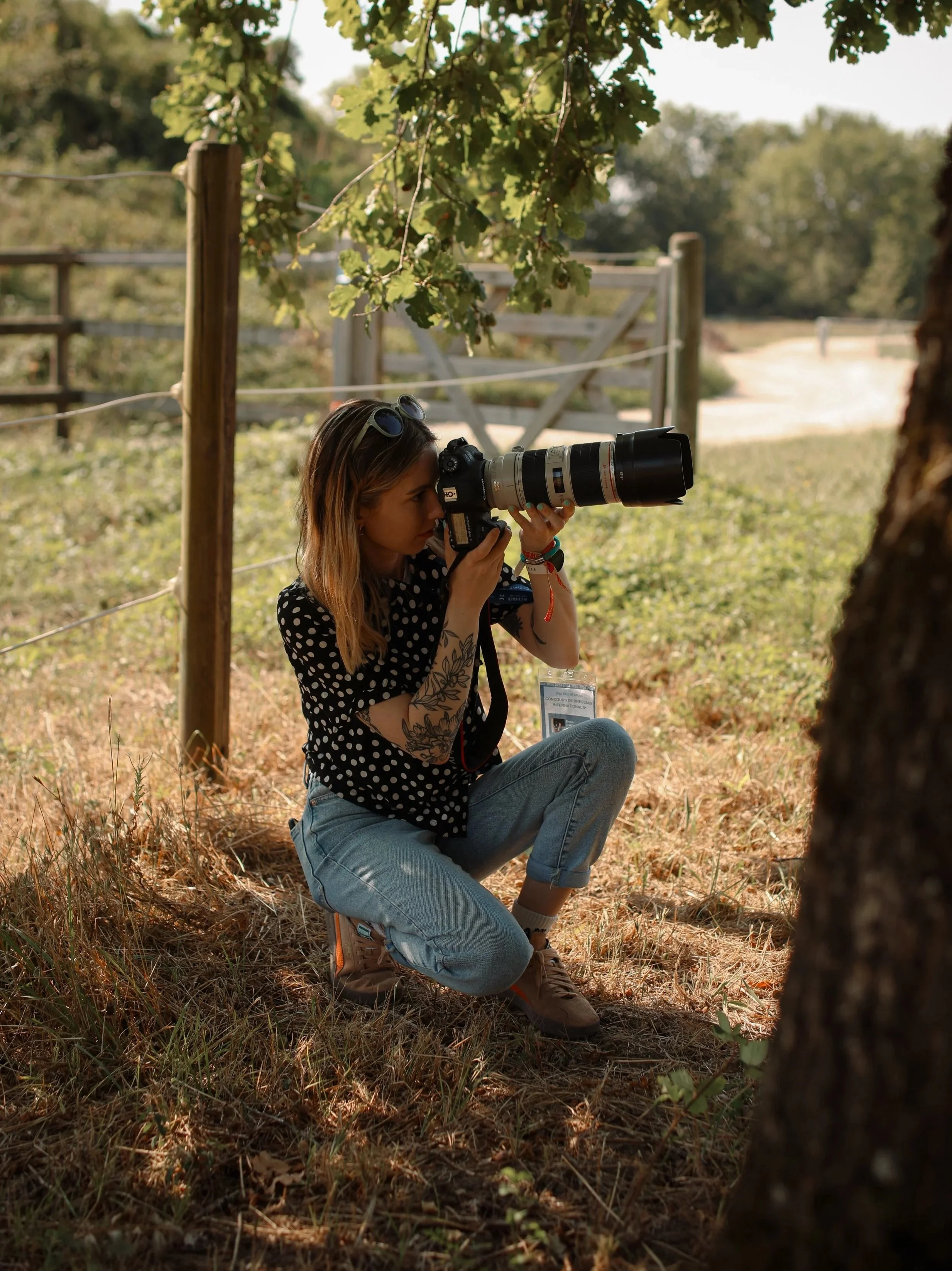 Em from Bolt&Bay Media kneeling taking candid photos from behind a tree of famous equestrian riders in a lifestyle shoot.