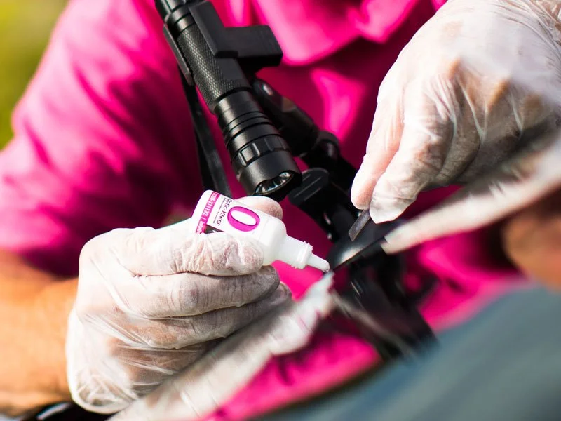 Close-up of a person wearing pink clothing and white gloves, injecting medication or vaccine into a firearm or similar device.