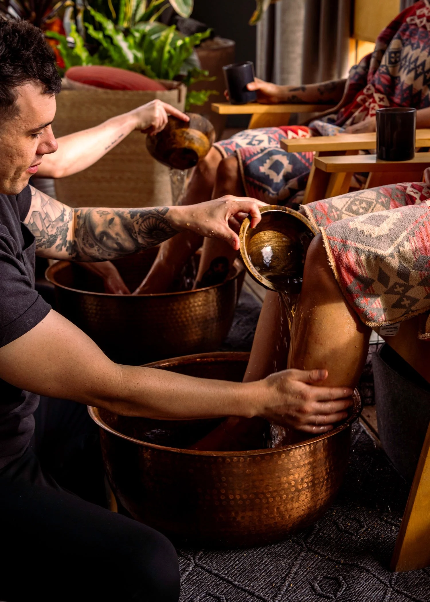 Hands pour water from a wooden bowl onto onto a person's shins, performing a foot rub treatment at Knot Springs