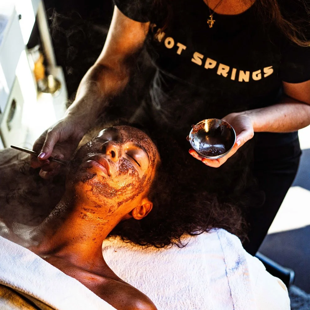A woman lying on a massage bed while a facial treatment is applied to her face