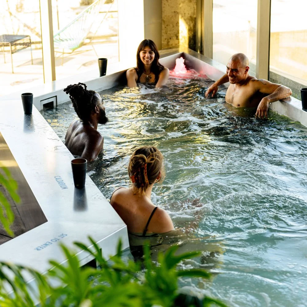 Four people sitting in a hot tub in front of a sunny window