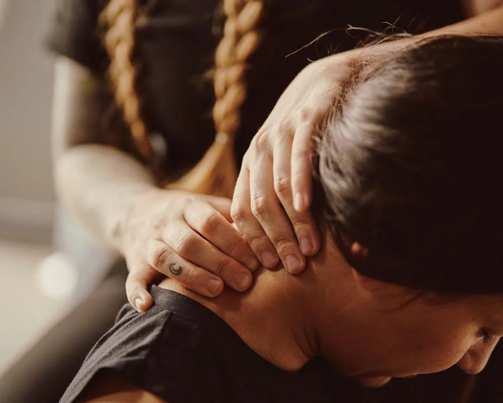A close up of a woman receiving a two-handed neck massage from a massage therapist