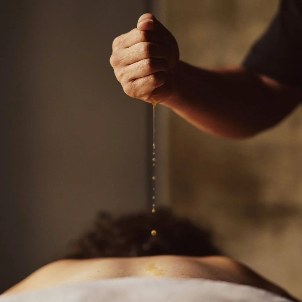 A hand slowly drops CBD oil over a person's back for a CBD massage.