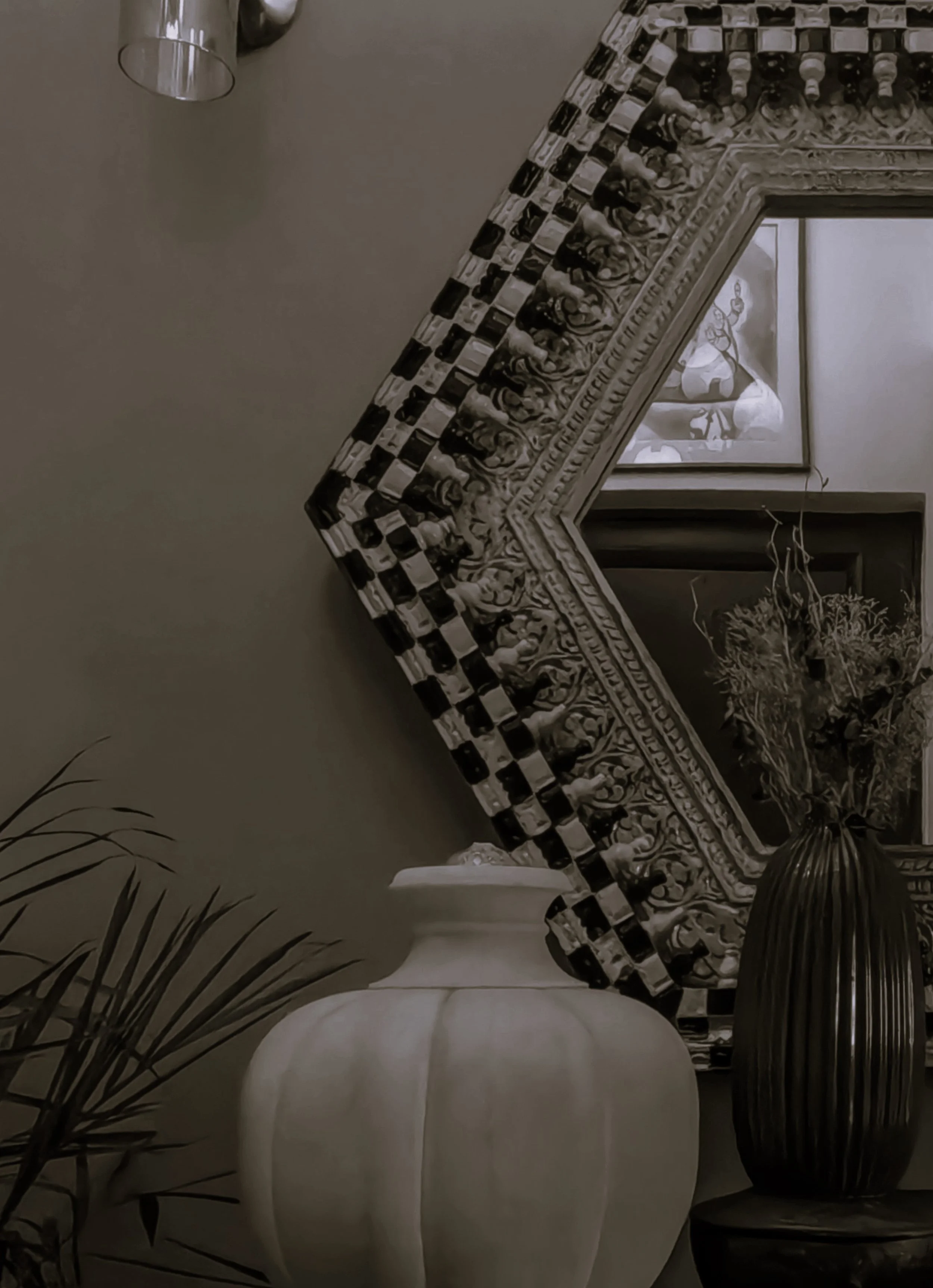 Decorative interior setting with a large white vase, a dark striped vase with flowers, and ornate frame with artwork on a wall.