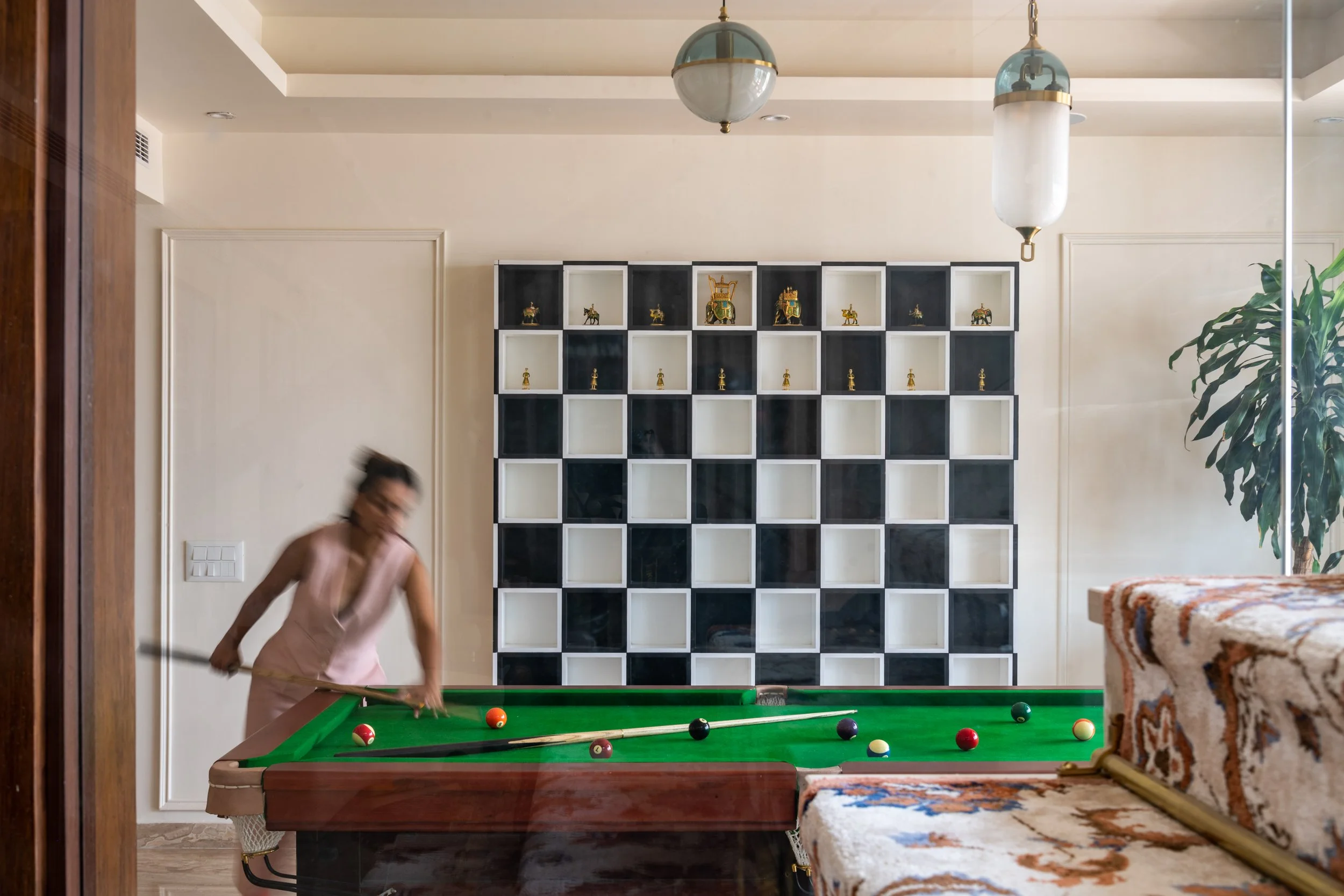 Person in pink dress playing pool inside a room with decorative shelving and a patterned couch.