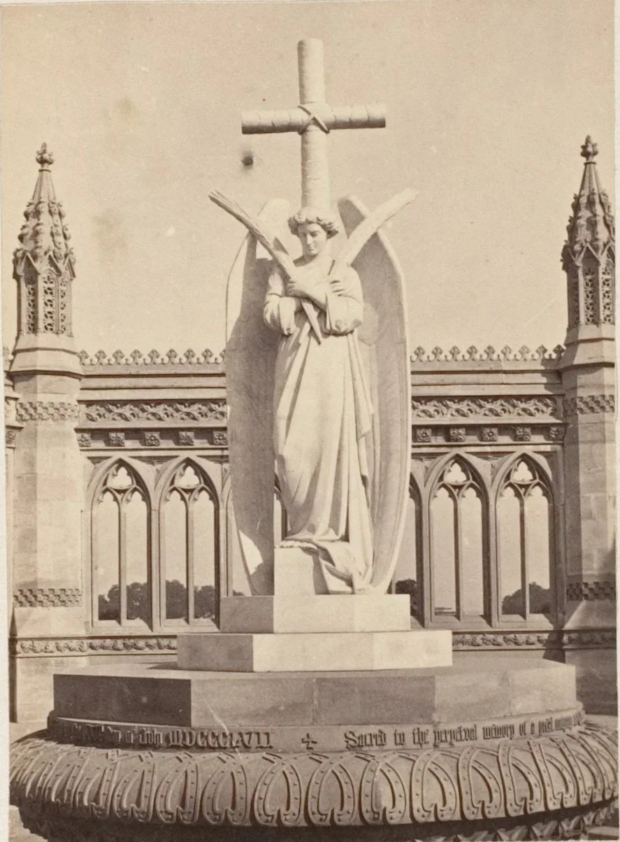 A vintage statue of an angel on a podium with a crucifix behind them