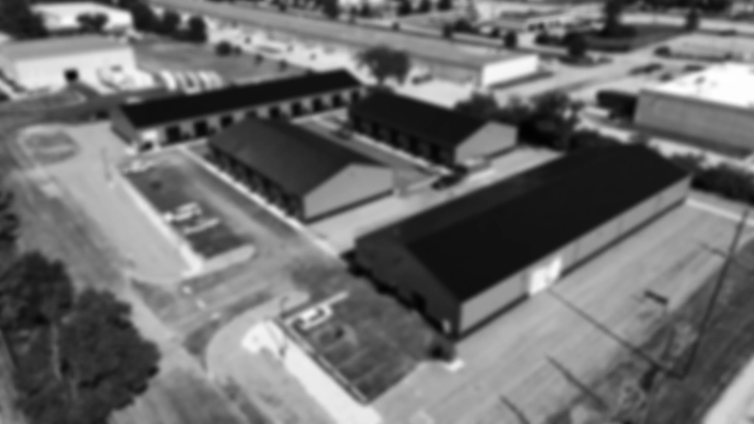 Blurry aerial black and white image of industrial buildings with parking lots and roads.