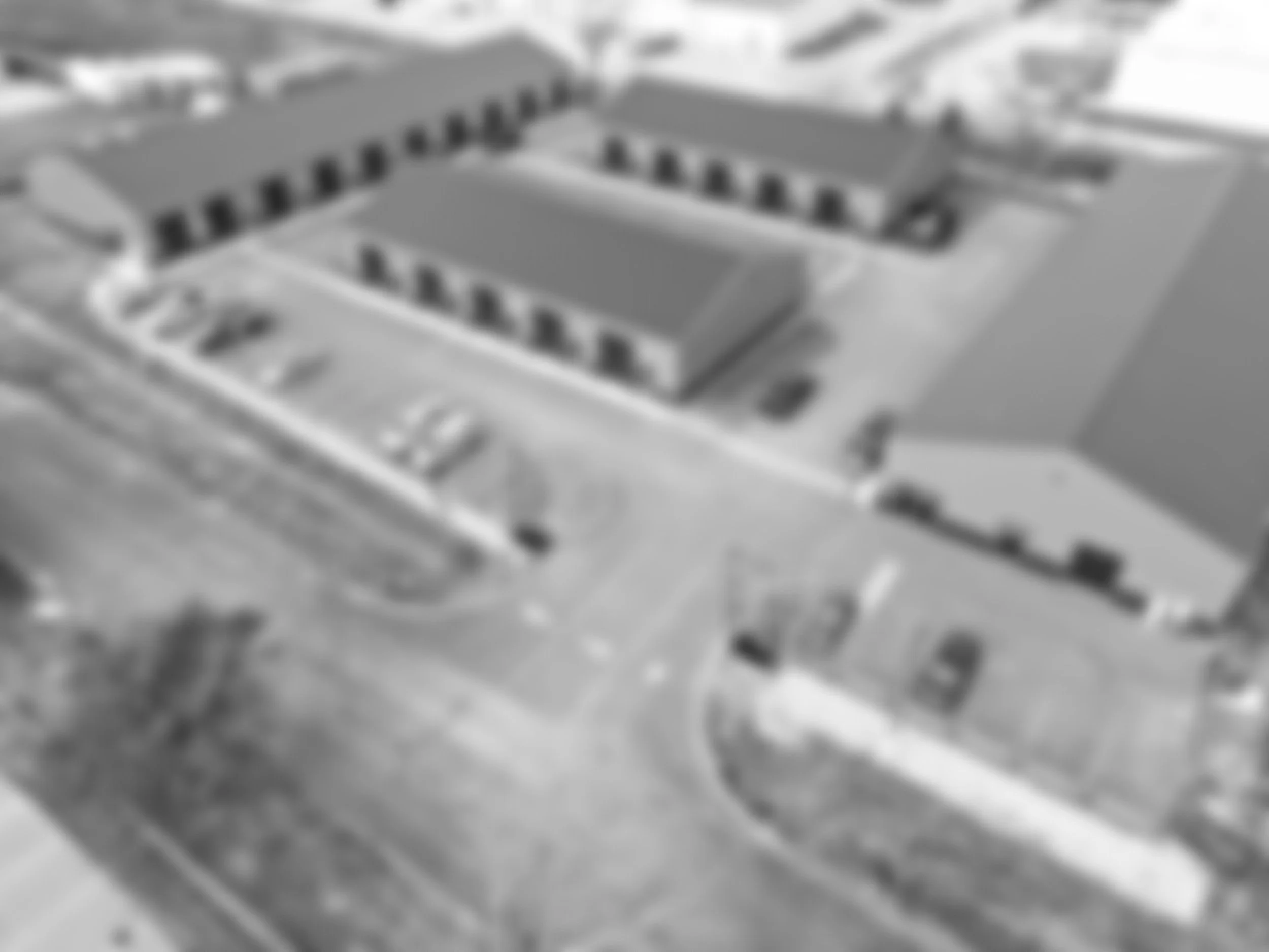 Aerial view of a large building complex with multiple interconnected buildings, parking lot, and surrounding roads.