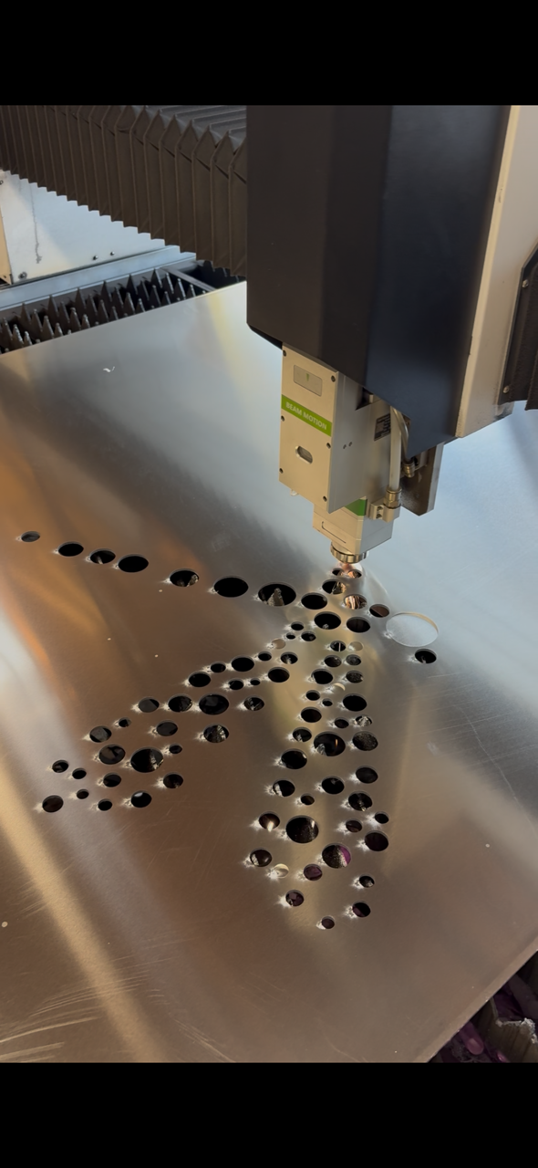 A laser engraving machine etching a pattern onto a metallic surface with several holes and circular designs.