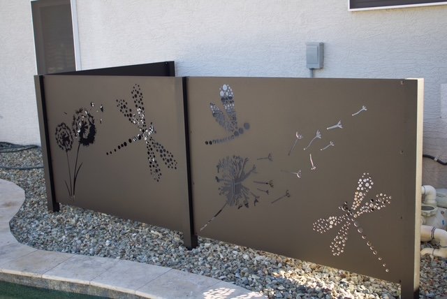 Decorative metal fence with cut-out dragonflies, flowers, and a bird design.
