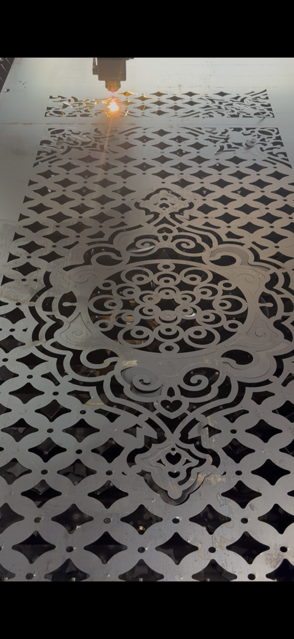 Laser cutting machine engraving intricate patterns on metal sheet with sun reflection.