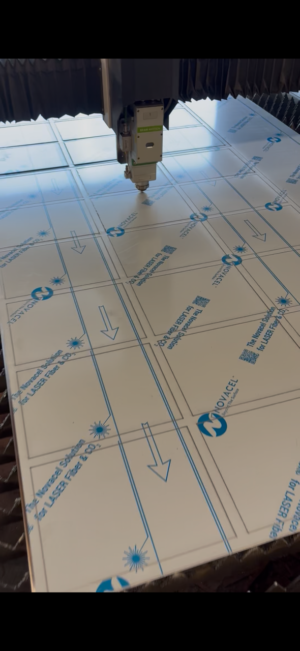 A laser cutter engraving a design onto a flat sheet of material labeled with the NOVACEL logo and instructions for use.