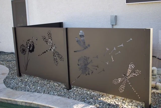 Decorative metal fence panels with dragonfly and flower cutouts beside a building.