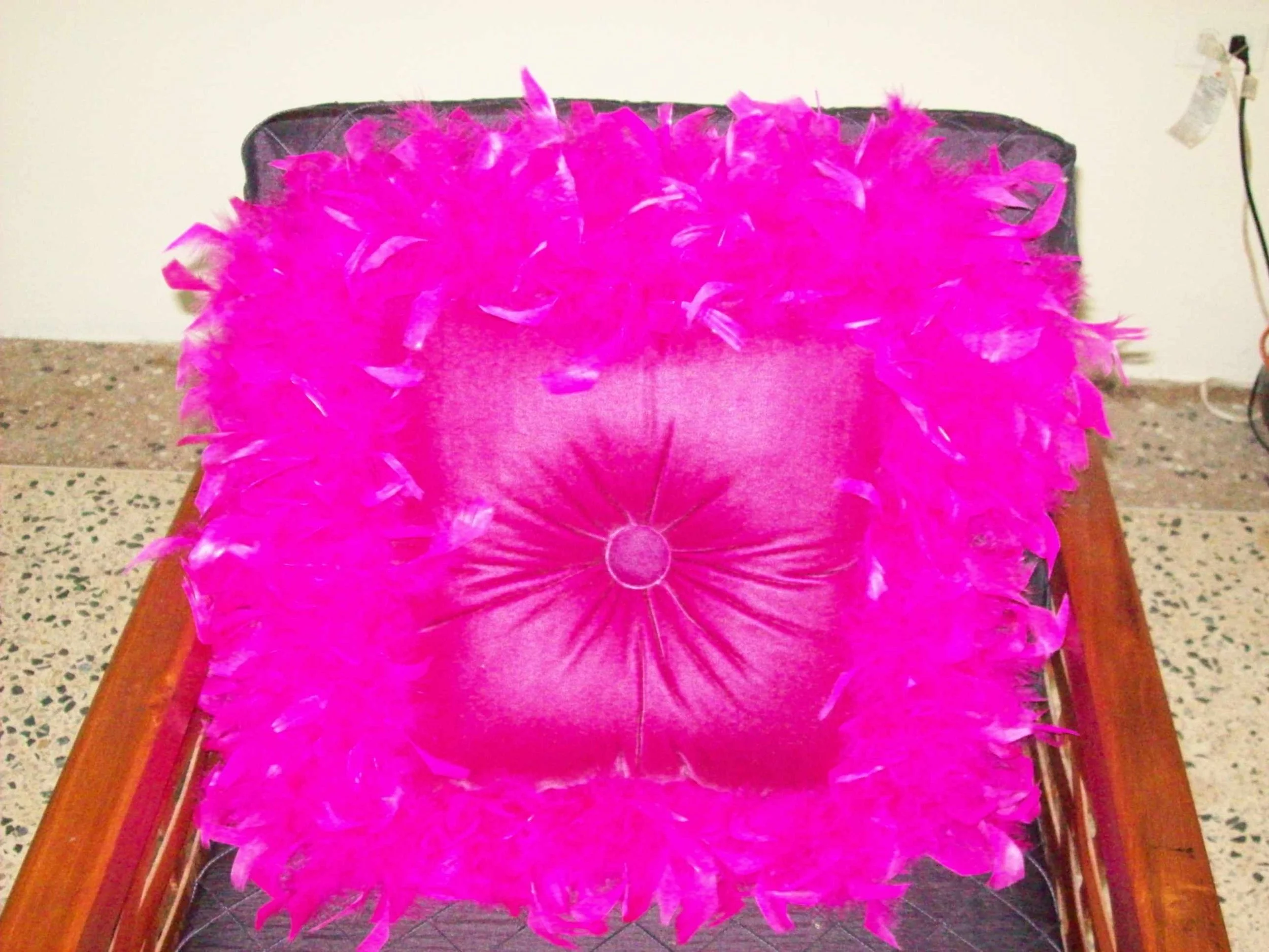 Pink feathered decorative pillow on a wooden chair.