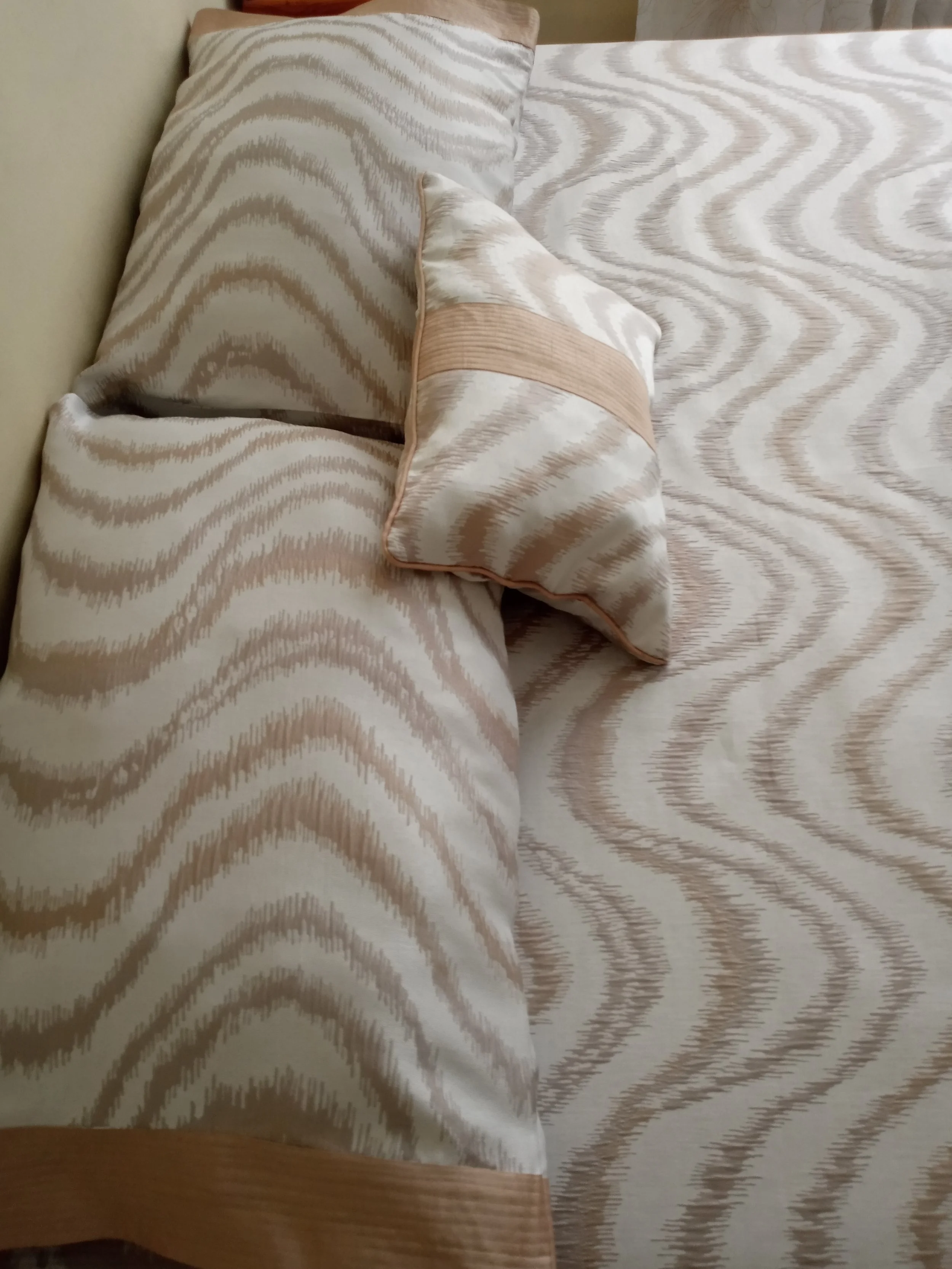 A bed with beige and white animal print bedspread and matching pillowcases, with a cushion resting on the bed.
