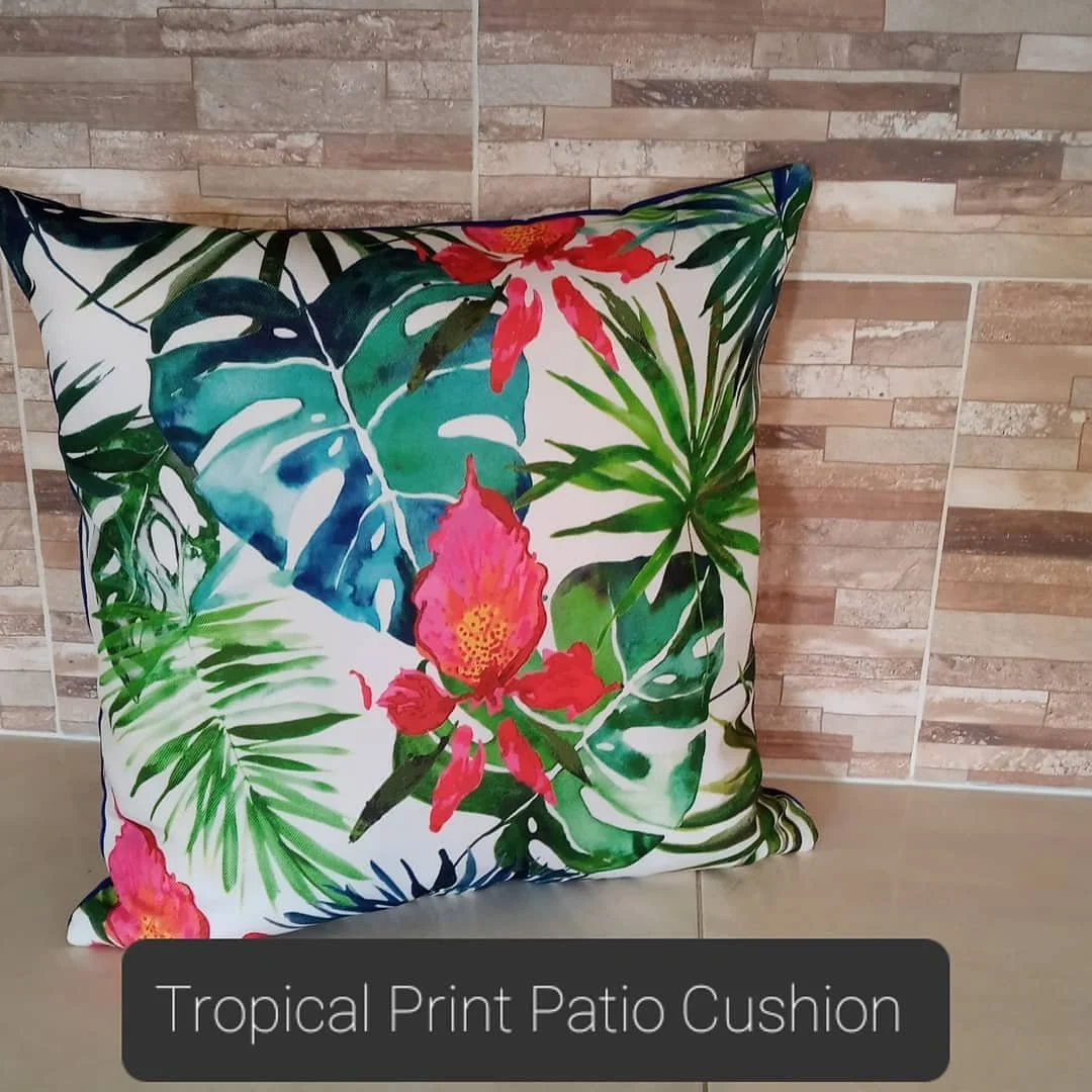 A decorative pillow with a tropical print featuring large green leaves and red-pink flowers, placed against a tiled wall.