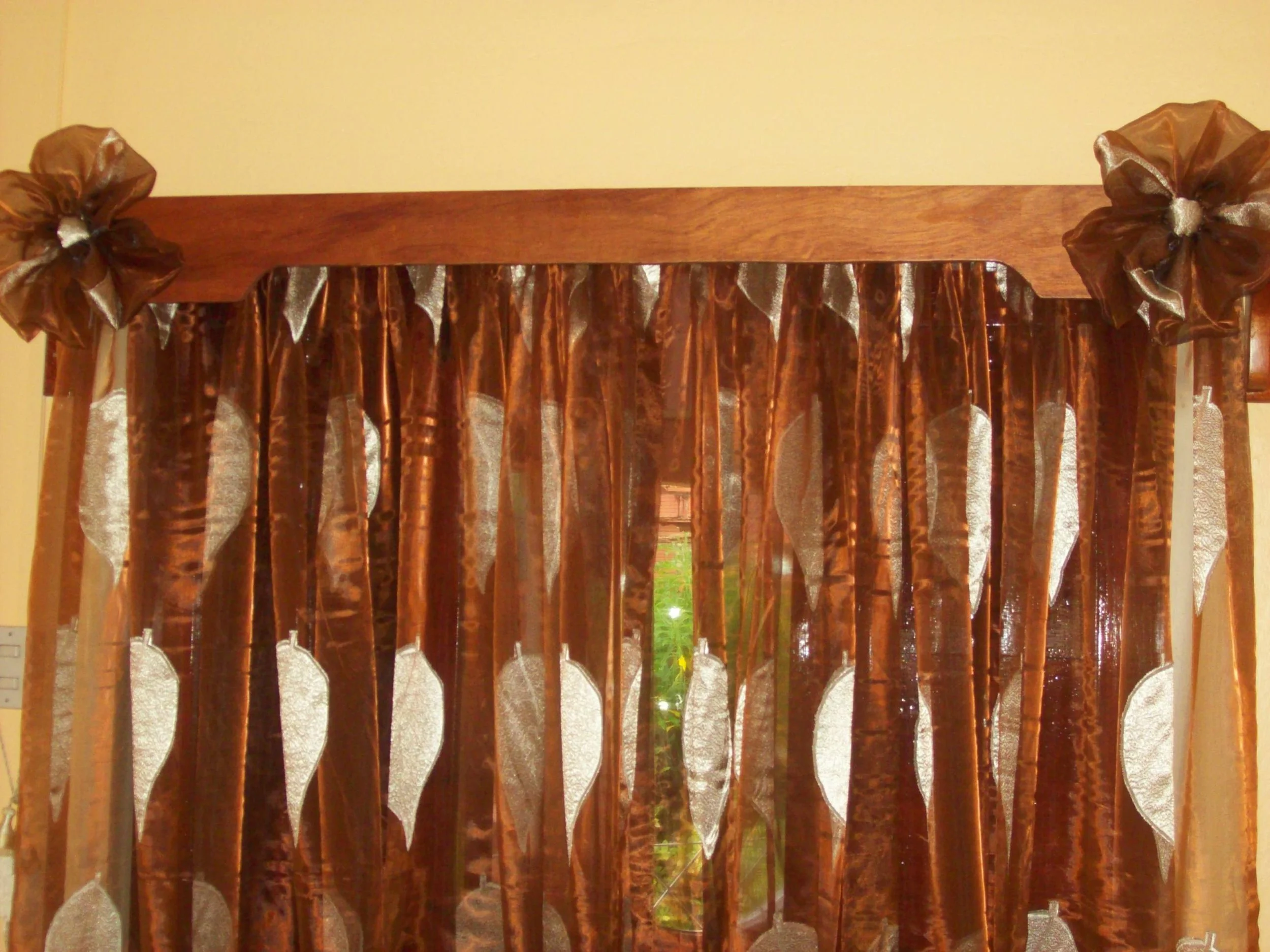 Brown curtains with white leaf patterns covering a window, tied with matching ribbon bows on either side.