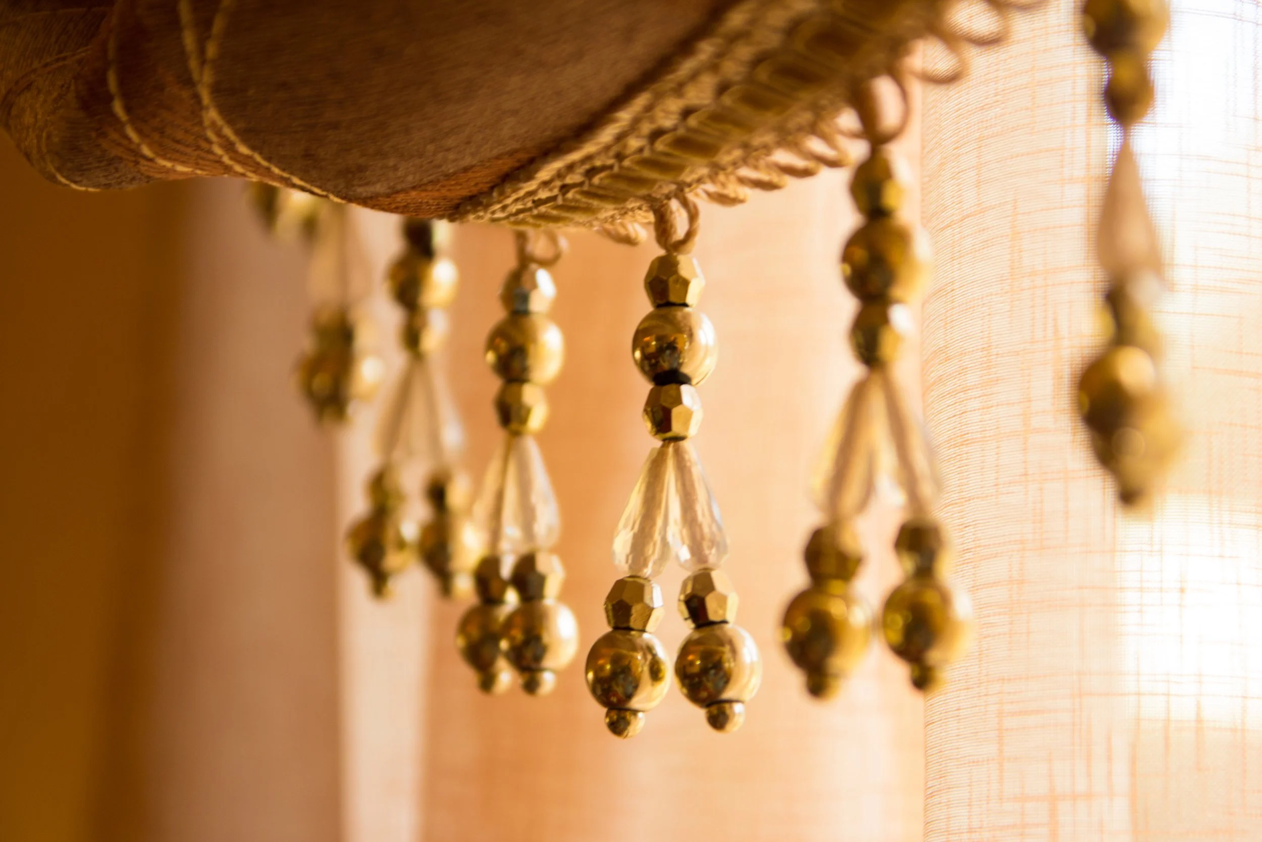Close-up of a chandelier with hanging beads and crystals, soft warm lighting, and a beige fabric lampshade in the background.