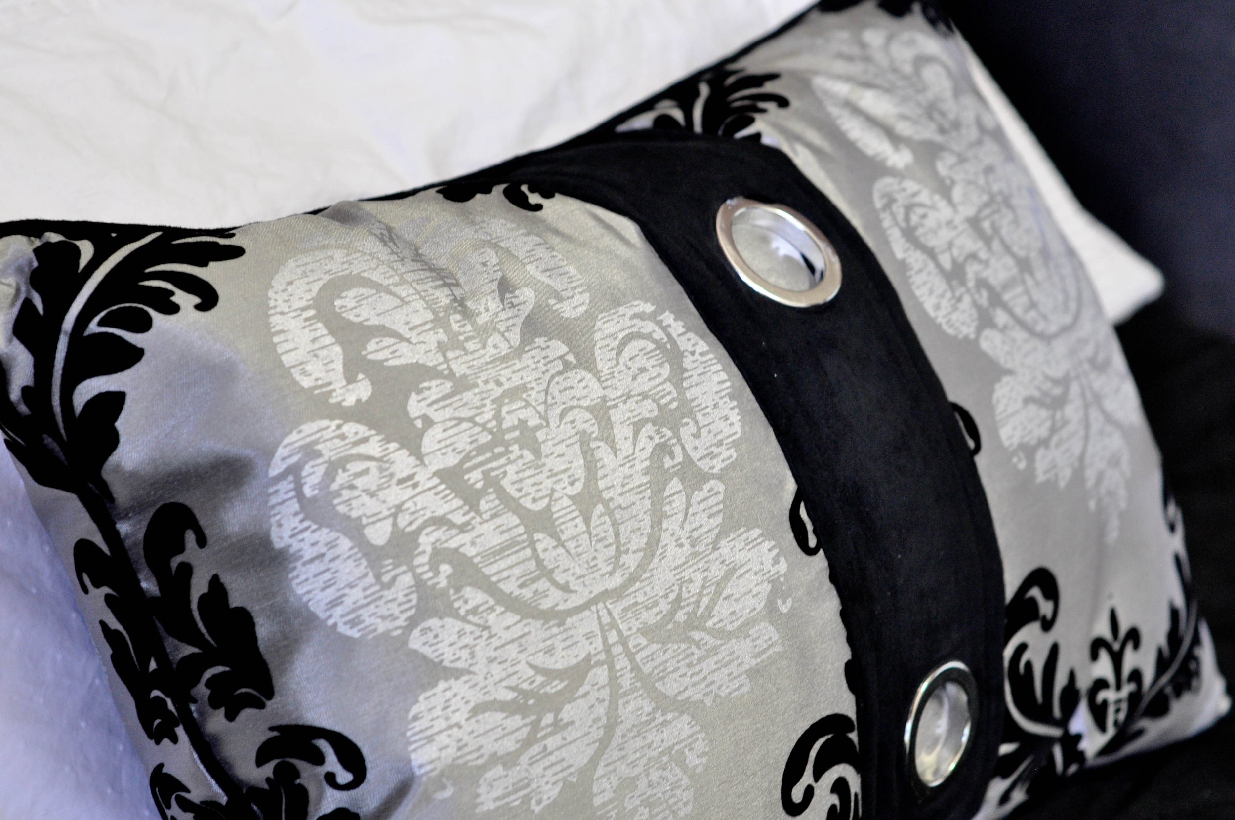 Close-up of a pillow with black and white floral and leaf pattern, featuring a black strap with metal grommets.