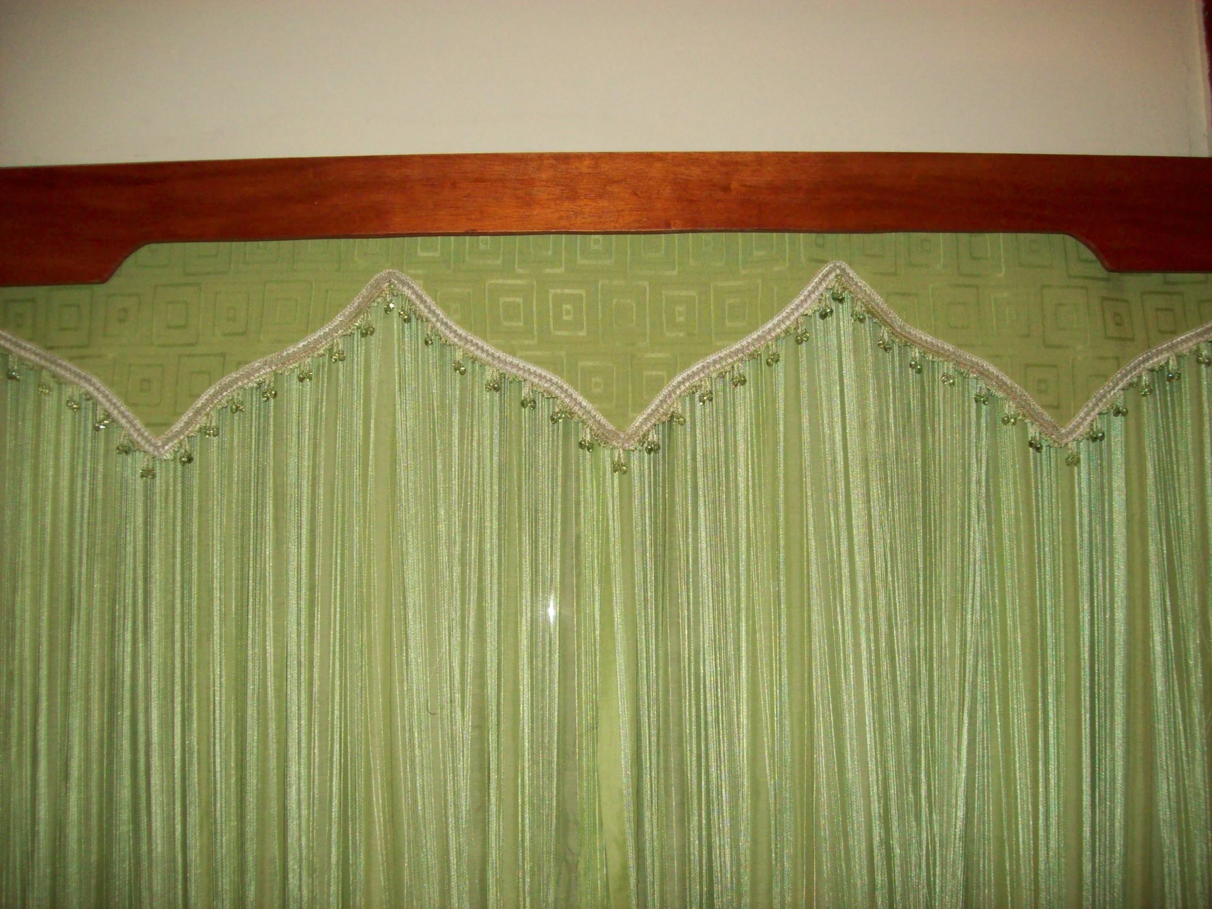 Green curtain with decorative trim hanging from a wooden headboard above a bed.