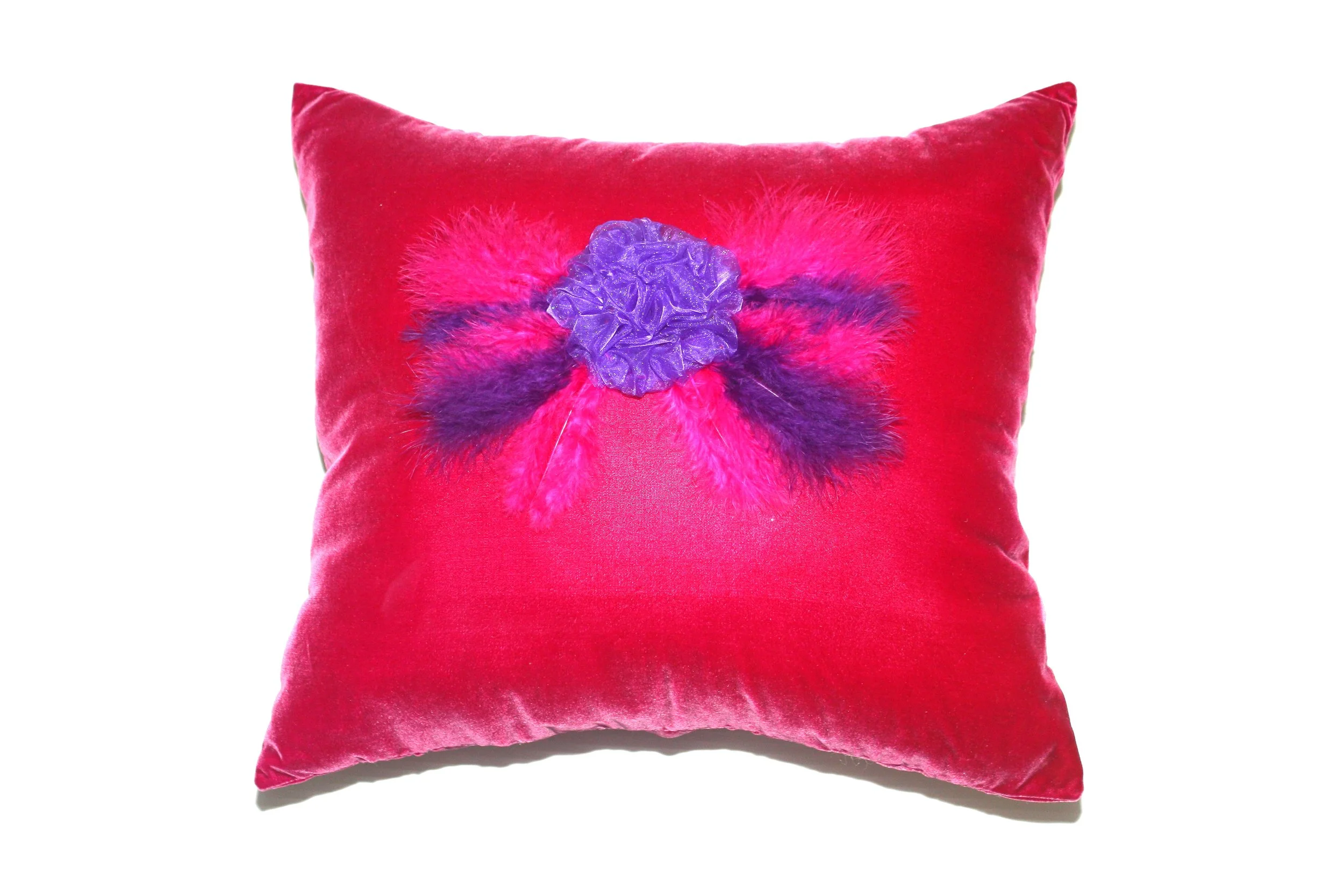 Red velvet throw pillow with a purple and pink feathered butterfly embellishment in the center.