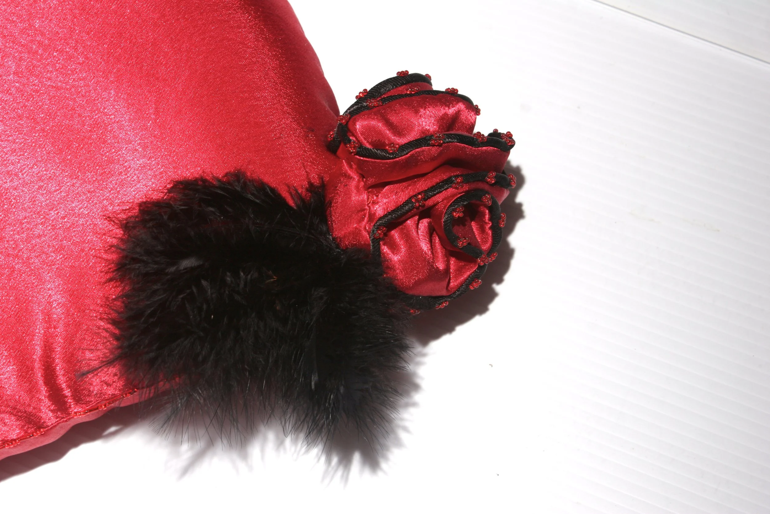Close-up of a red satin garment with black feathered embellishment on a white textured surface.