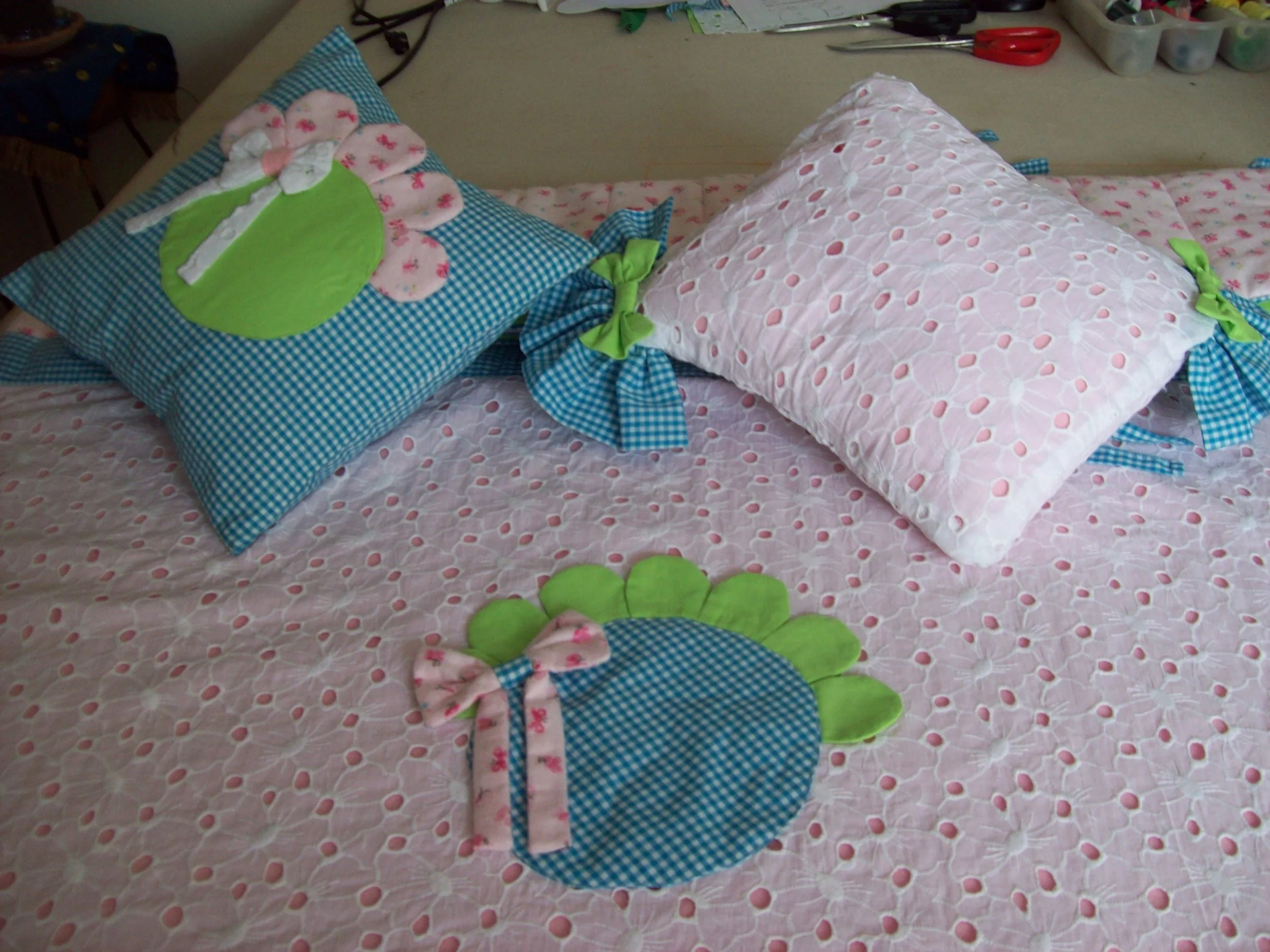 Two decorative pillows on a pink bedspread, one with a chicken applique and the other with a pink quilted pattern, and a green and blue chicken placemat with a pink bow in front of them.