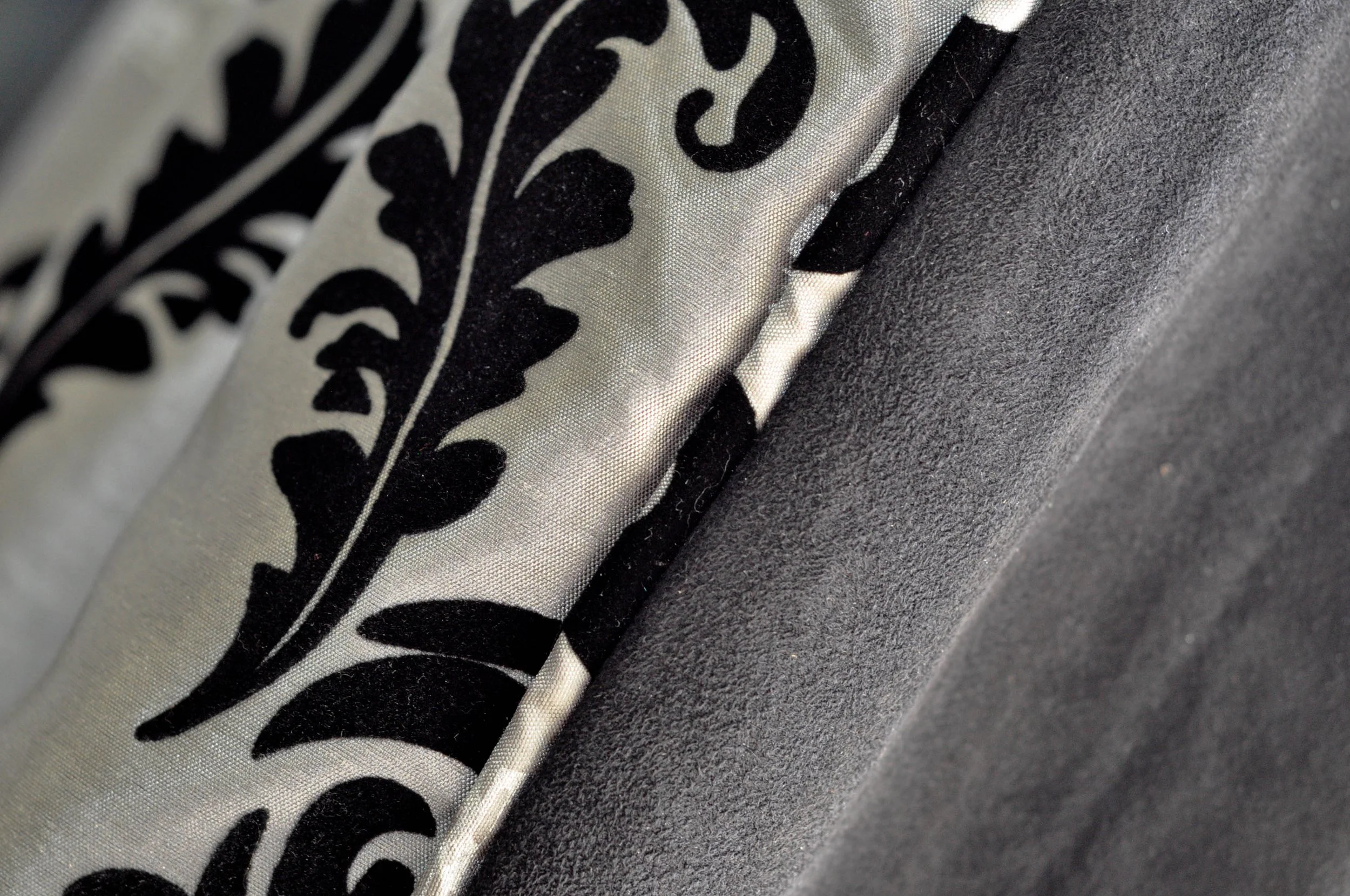 Close-up of a black and white fabric with a floral or leaf pattern, contrasting with a plain dark fabric.