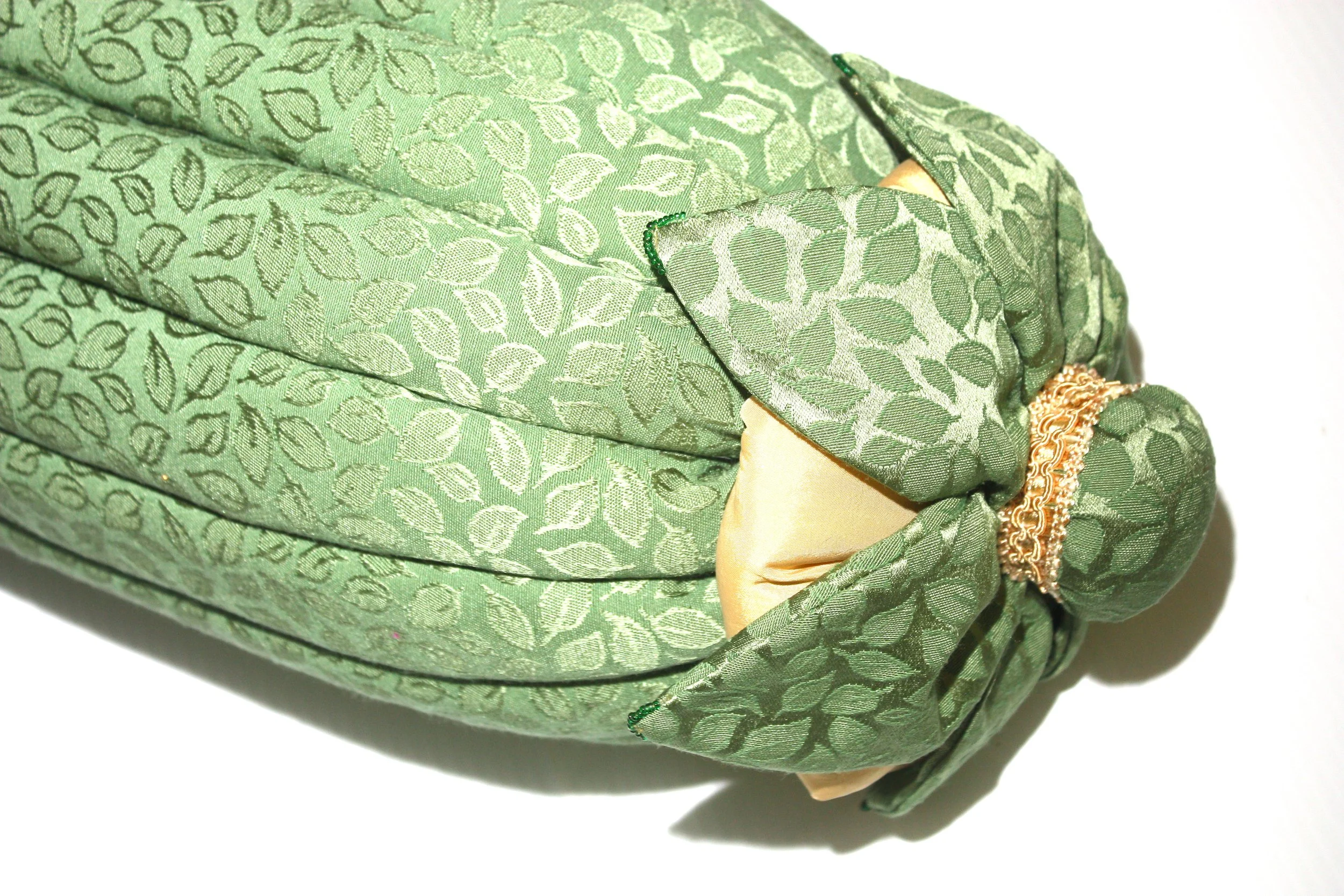 A fabric pouch or bag made of green patterned material with leaf designs, gathered at one end with a gold-colored decorative band.