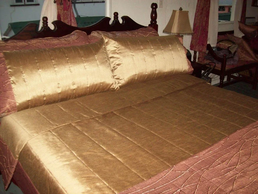 Queen-sized bed with gold satin bedspread and matching pillows in a vintage bedroom.