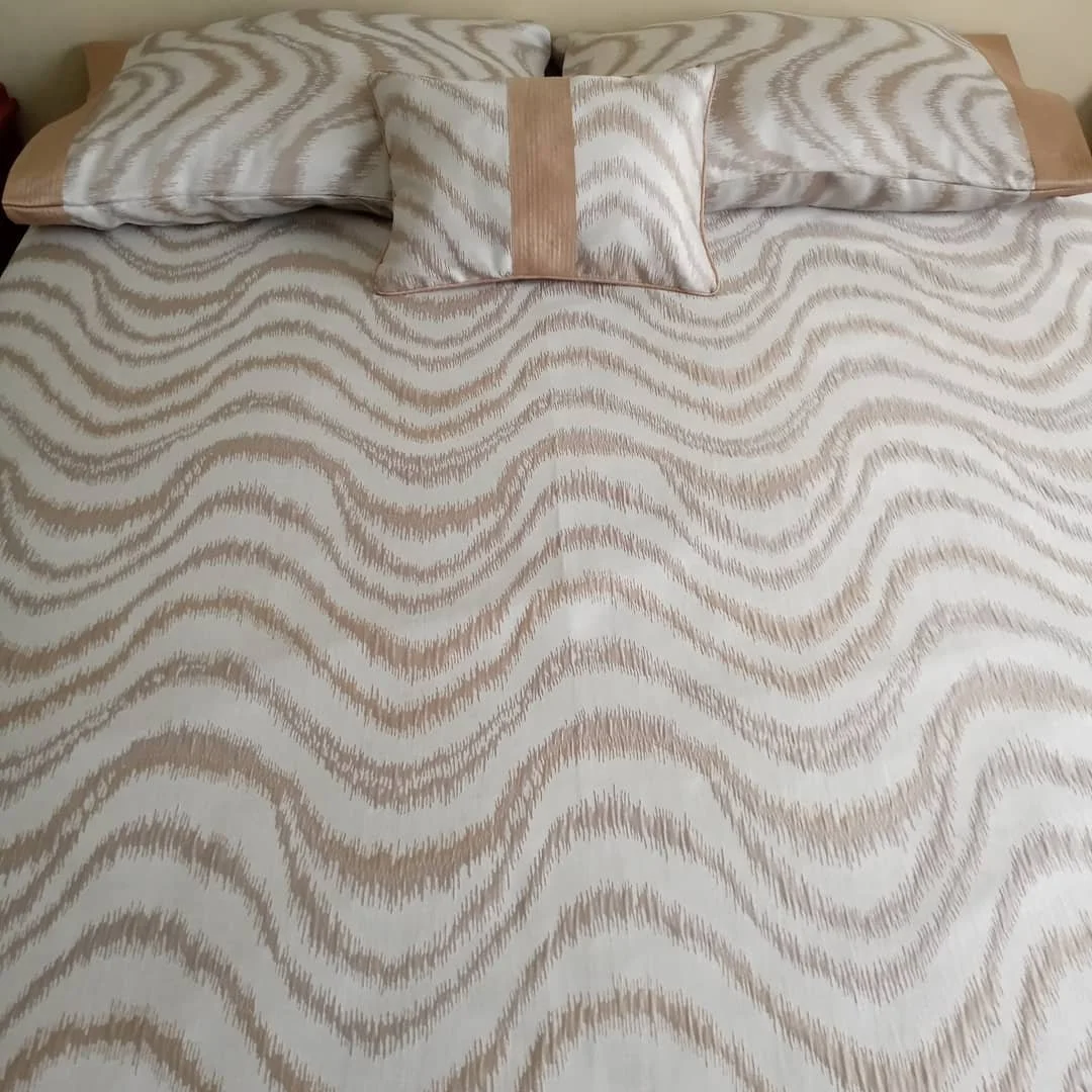 A bed with a white and beige patterned bedspread and matching pillows with a wave-like design.