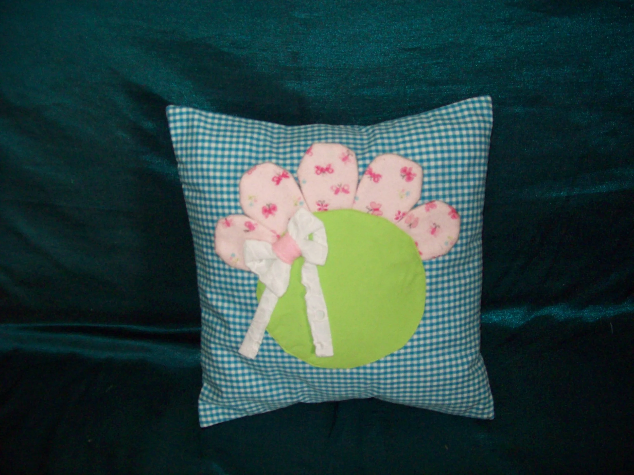 Decorative pillow with a apple shape and pink flowered petal design, white bow, and blue gingham background.