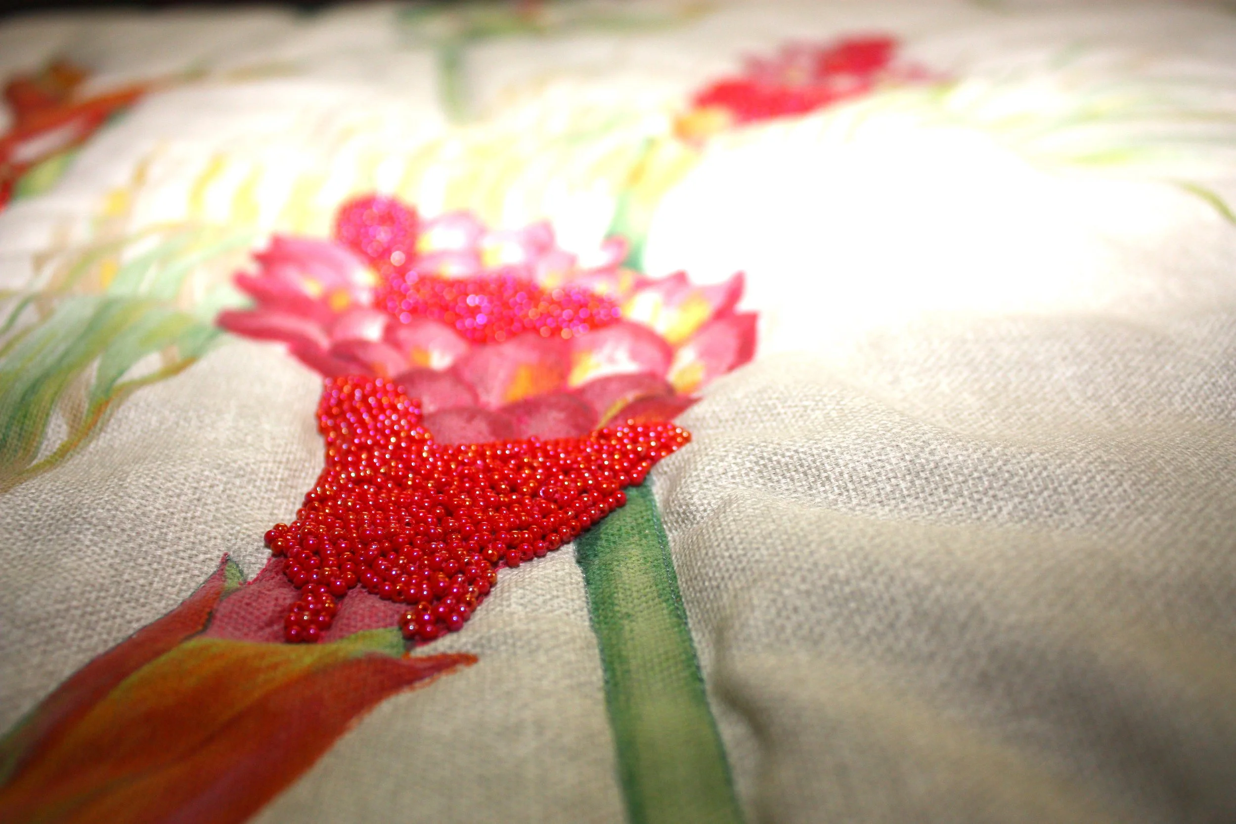 Close-up of a fabric with a painted floral design and red bead embellishments.