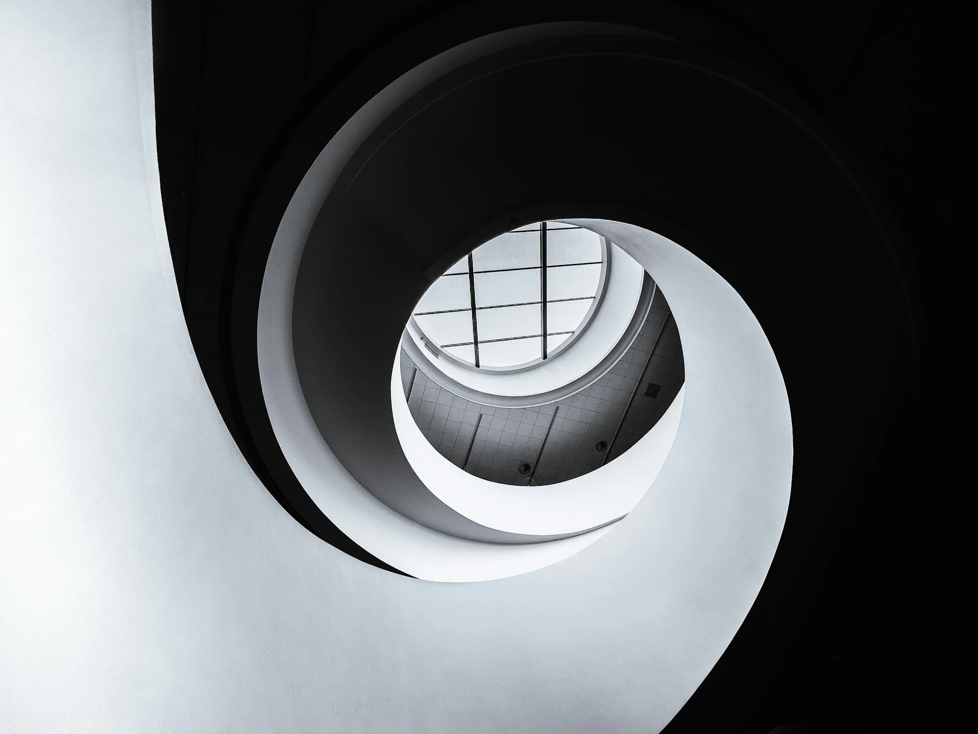 View looking up a spiral staircase with a glass ceiling.