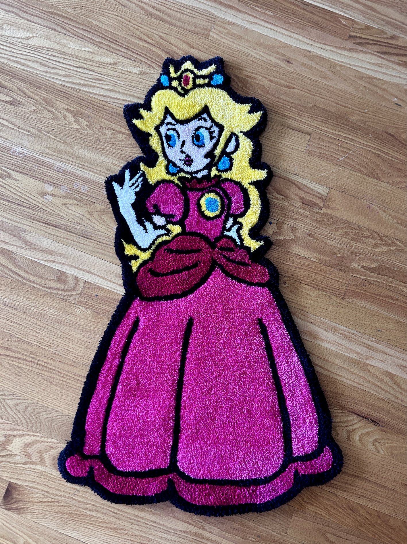 Colorful rug featuring Princess Peach from the Mario video game series, with blonde hair, a crown, and a pink dress, on a wooden floor.