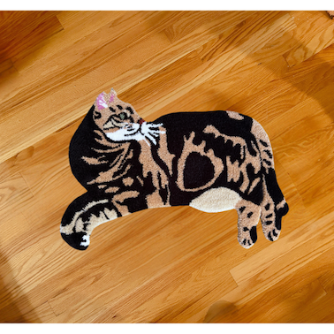 A cat-shaped rug with a tabby cat lying down, facing left, with brown and black stripes and white details.