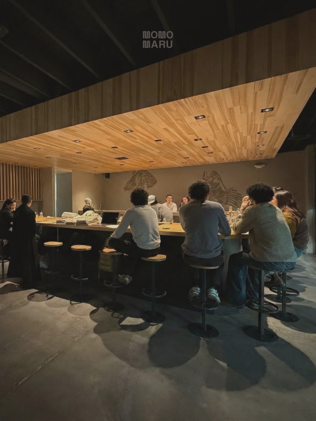People sitting around Momomaru hand roll sushi bar, engaged in conversation.