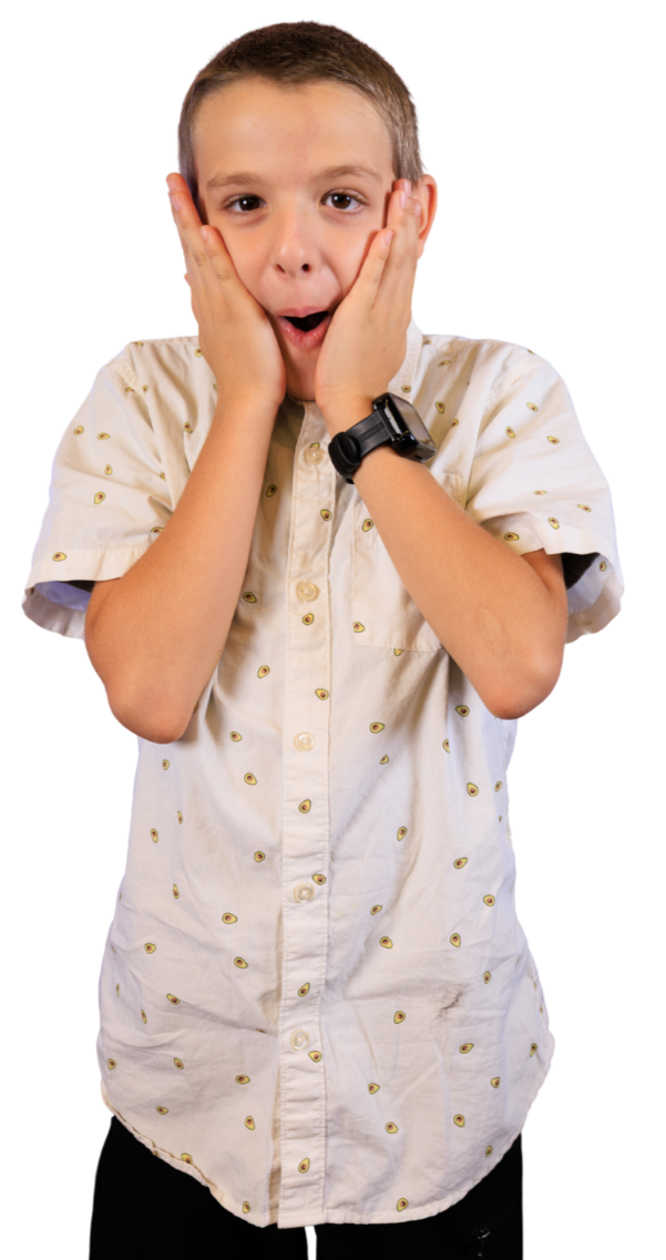 A boy with short hair wearing a beige shirt with small printed designs, holding his face with both hands, and displaying a surprised or shocked expression.